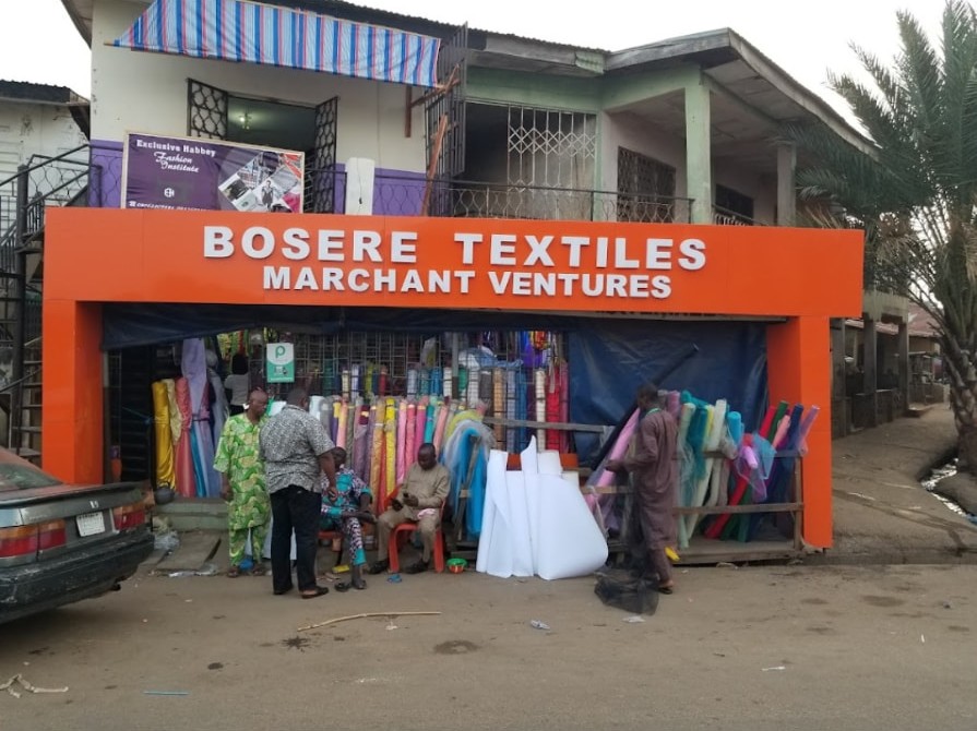 The Bosere Textiles Merchant Ventures storefront in Ilorin, with rolls of fabric on display and customers outside the shop.