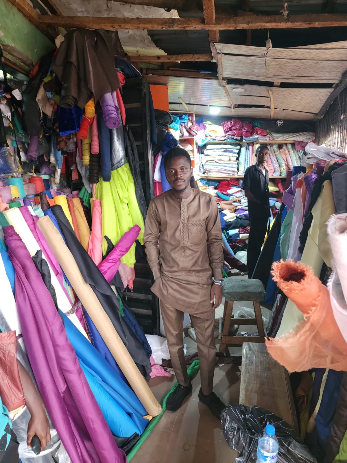 Inside the Bosere Textile shop: two people standing among floor-to-ceiling stacks and rolls of fabric.